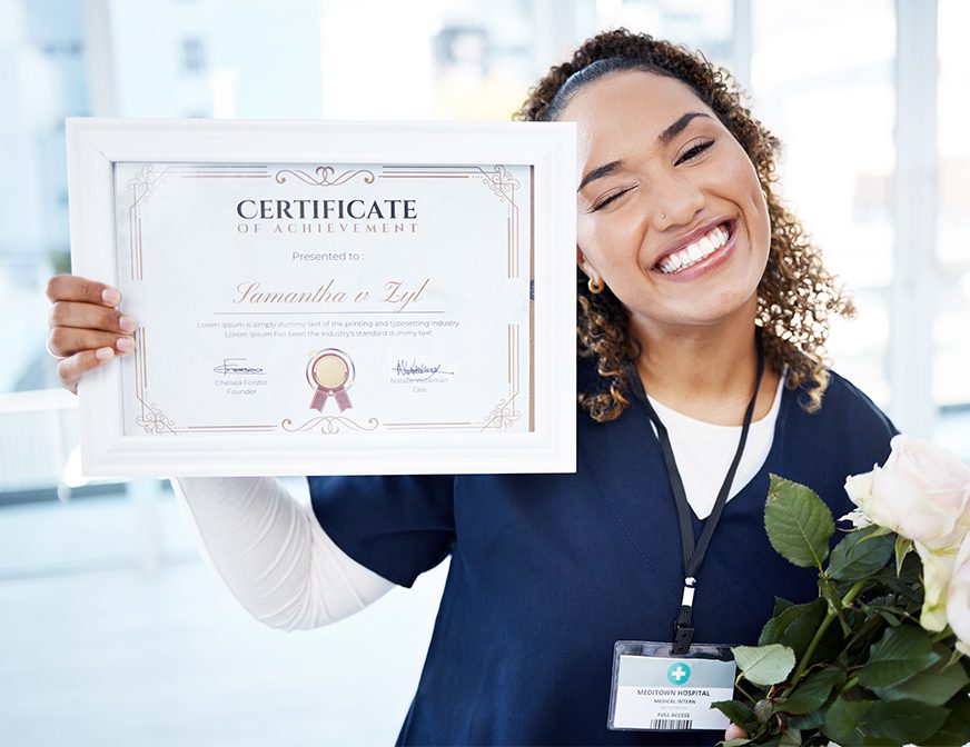 Smiling woman in scrubs holds a bouquet of white roses and a framed certificate of achievement, with her hospital staff badge visible.